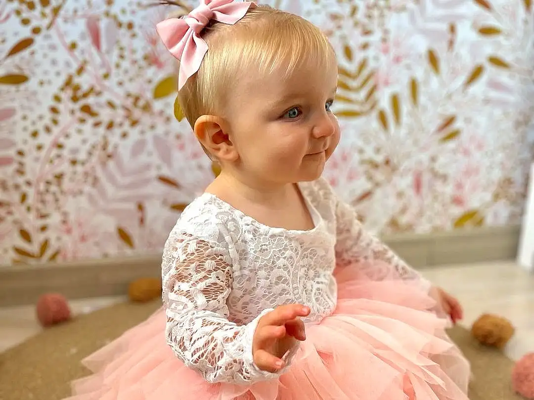 Blanc, Dress, Sourire, Baby & Toddler Clothing, Sleeve, Rose, Happy, Embellishment, Bambin, Headpiece, Enfant, Magenta, Day Dress, Pattern, Peach, Event, Hair Accessory, Fashion Accessory, Formal Wear, Ruffle, Personne