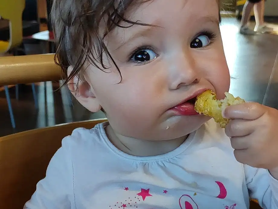 Nez, Joue, Peau, Nourriture, Baby Playing With Food, Facial Expression, Tableware, Mouth, Food Craving, Yellow, Baby, Bambin, Chair, Cuisine, Biting, Drinkware, Sweetness, Enfant, Comfort Food, Junk Food, Personne