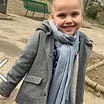 Visage, Head, Yeux, Sourire, Plante, Sleeve, Arbre, Jacket, Overcoat, Bambin, Herbe, Enfant, Pattern, Blond, Bench, Scarf, Poil, Leisure, Wool, Fashion Accessory, Personne, Joy
