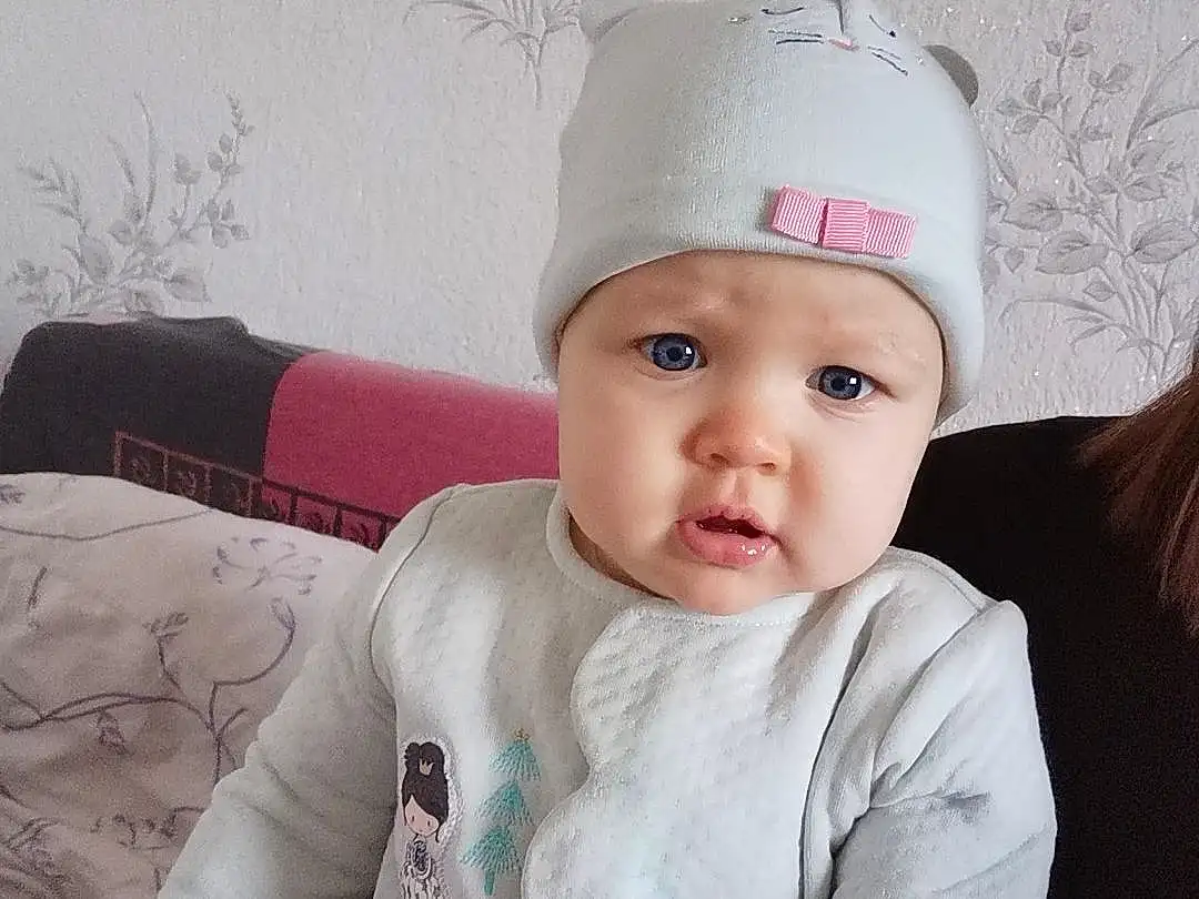 Joue, Head, Lip, Chin, Neck, Textile, Sleeve, Comfort, Cap, Baby & Toddler Clothing, Baby, Rose, Bambin, Flash Photography, Knee, Enfant, Fashion Accessory, Human Leg, Room, Beanie, Personne, Headwear