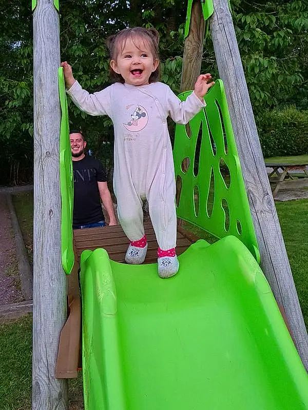 Sourire, Photograph, Green, Arbre, Chute, Plante, Playground Slide, Aire de jeux, Herbe, Leisure, Fun, People In Nature, Woody Plant, Happy, Outdoor Play Equipment, Recreation, Bambin, City, Enfant, Baby & Toddler Clothing, Personne, Joy